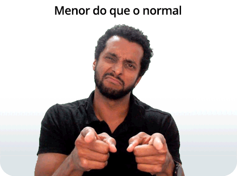 Composição com texto e fotografia. Na parte superior, está escrito “Menor do que o normal” em letras pretas. Abaixo, um homem de pele parda, cabelos cacheados, curtos e pretos, e barba preta, com o corpo voltado para frente e a cabeça levemente inclinada para a direita. Ele aparece do peito para cima, franze a testa, aperta os olhos e projeta os lábios cerrados e levemente estendidos lateralmente. Aponta para frente com os dois dedos indicadores, mantendo os demais dedos recolhidos.
